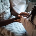 Female doctor holding hands of her patient in hospital room.