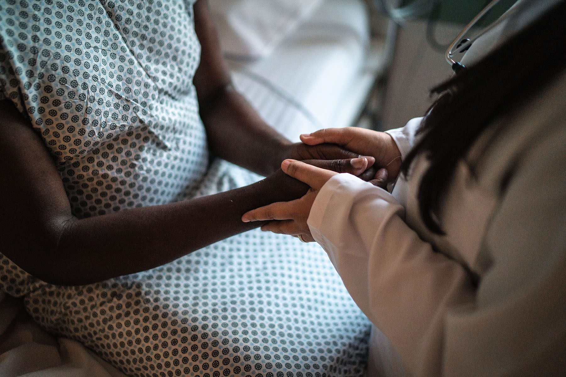 Female doctor holding hands of her patient in hospital room.