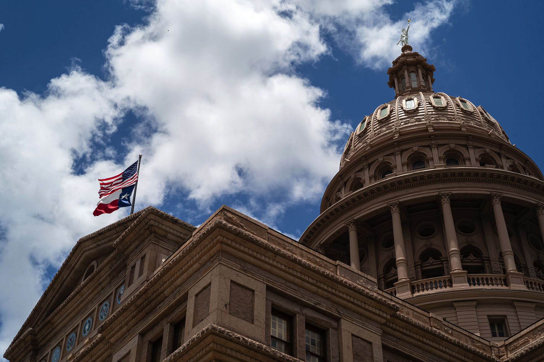 A U.S. and a Texas flag fly over the Texas State Capitol.