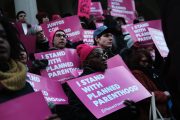 A diverse crowd of people hold signs that read 