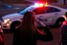 A woman salutes as a procession of police cars pass.