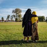 Afghan refugee girls hold each other as they watch a soccer game on an army base.