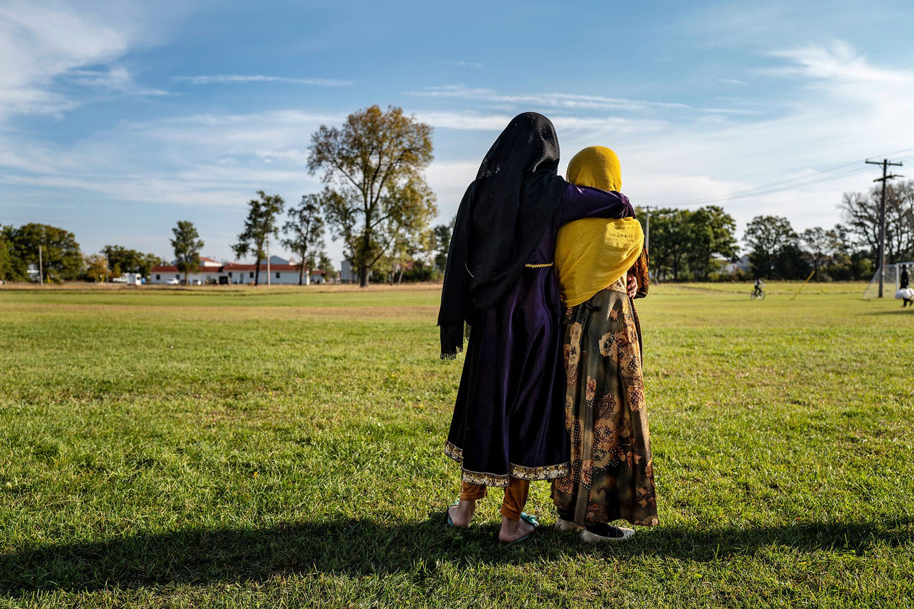 Afghan refugee girls hold each other as they watch a soccer game on an army base.