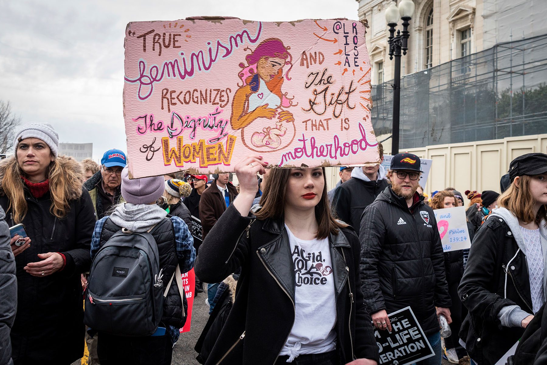 A woman holds up a sign that reads "true feminism recognizes the dignity of women and the gift that is motherhood."