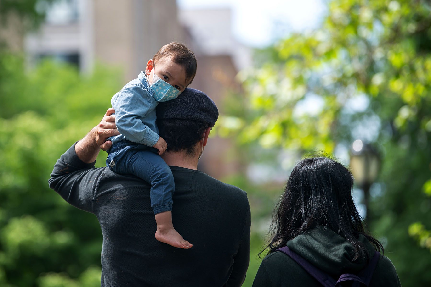 A dad holds his child on his shoulder during a family walk.