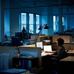 A woman works at her desk in empty office at night.