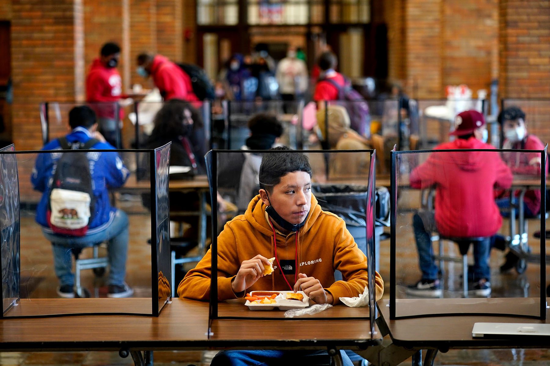 Students eat lunch separated from classmates by plastic dividers.