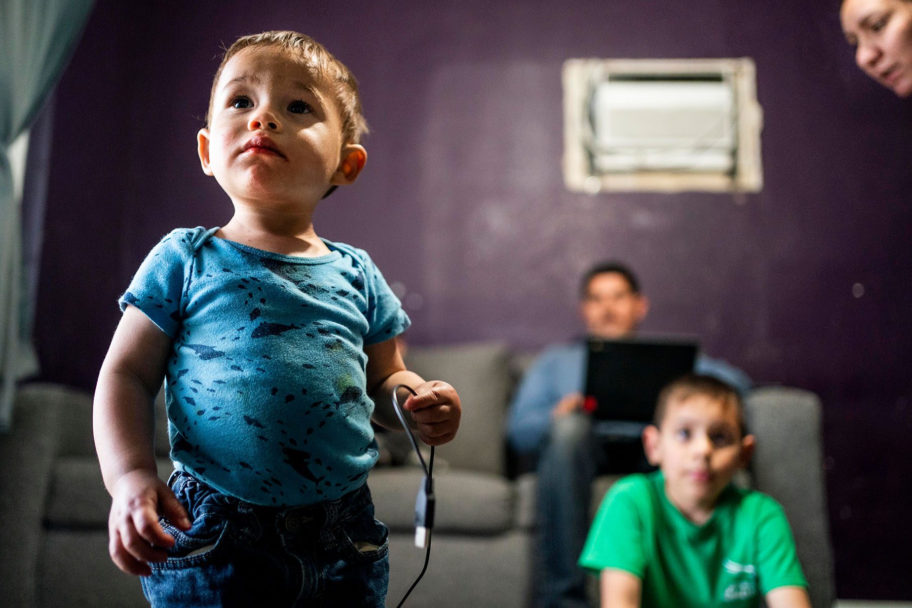 A family is seen in their living room. The smallest of the children is in focus.