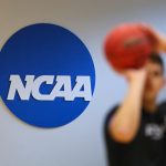 A person prepares to shoot a basketball standing in front of a NCAA logo.