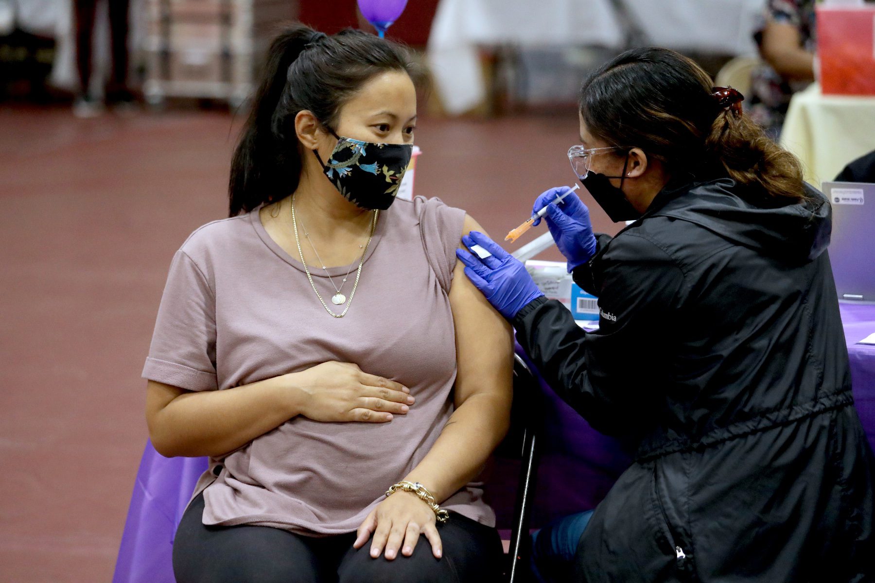 A pregnant person receives a COVID vaccine in her arm.