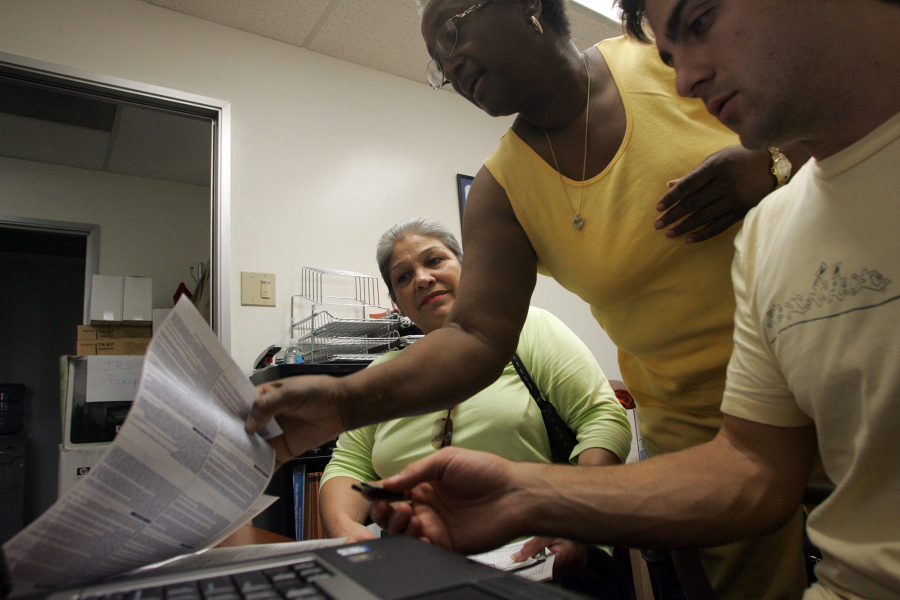 A woman receives help on her taxes by two volunteers sitting at a computer.