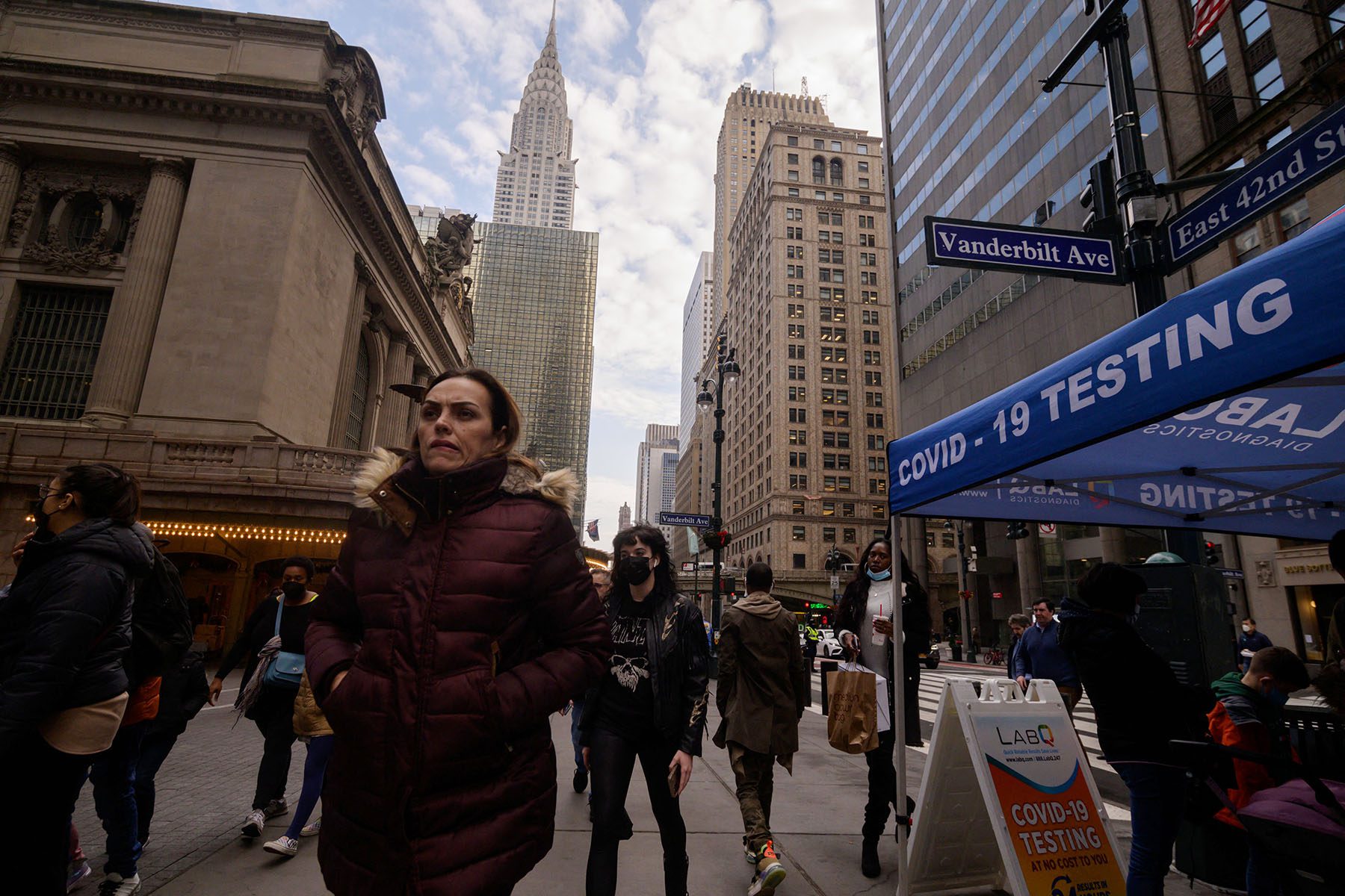 Pedestrians pass a covid-19 testing booth on a busy New York City street.