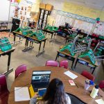 A teacher interacts with students virtually while sitting in an empty classroom.