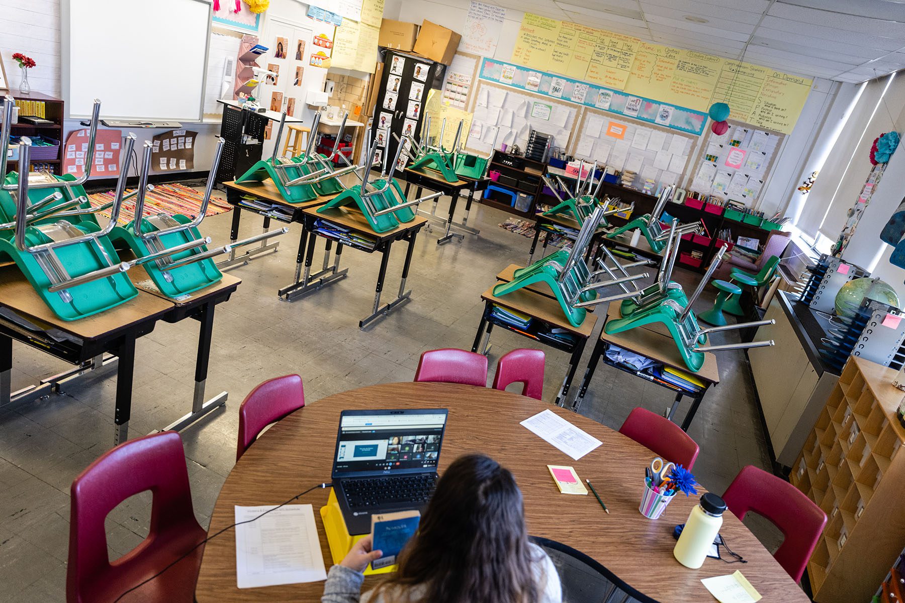 A teacher interacts with students virtually while sitting in an empty classroom.