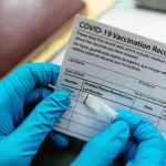 A nurse adds a label to a COVID-19 vaccination card