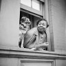 A woman and her dog take in the sights as they look out from their open window.