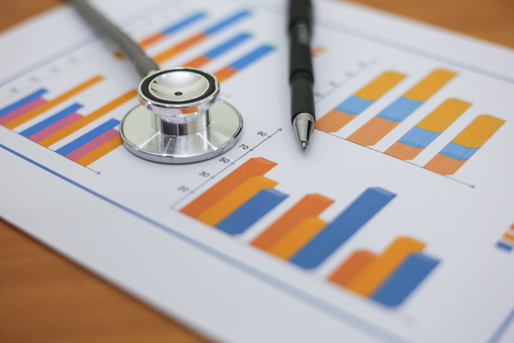 A stethoscope and pen lie on top of a paper with charts on it.