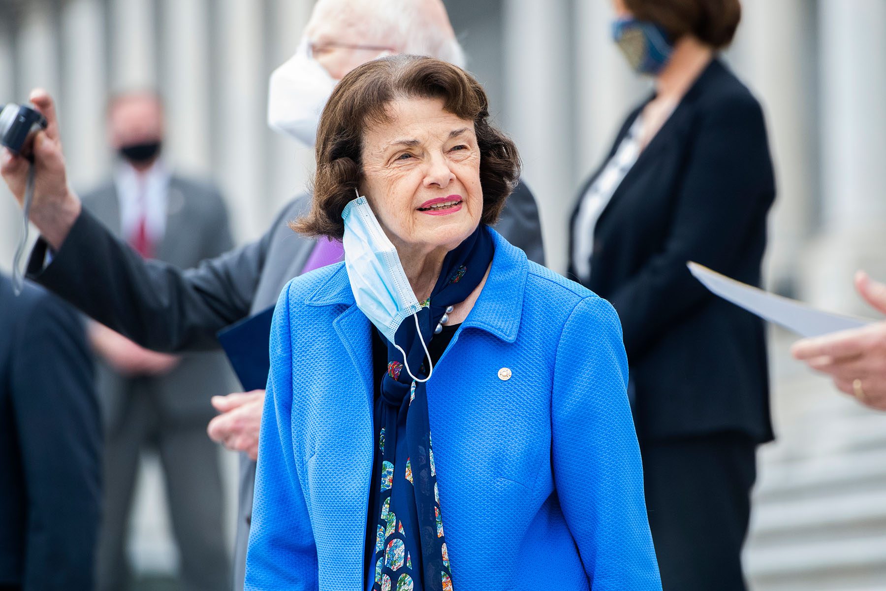 Dianne Feinstein looks into the distance from the steps of the Capitol as her face mask hangs from her ear.
