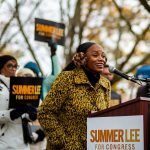 Summer Lee is seen smiling at a podium as people hold signs that read 