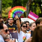 Members and supporters of the LGBTQ community, several of them holding flags and posters, attend the 