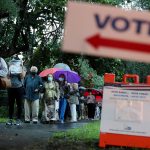 Voters wait in line to cast their ballots on a rainy florida morning. Several people in line are holding umbrellas and wearing face masks. A 