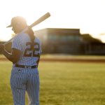 Rachel Balkovec in seen in full uniform holding a baseball bat on a baseball field.