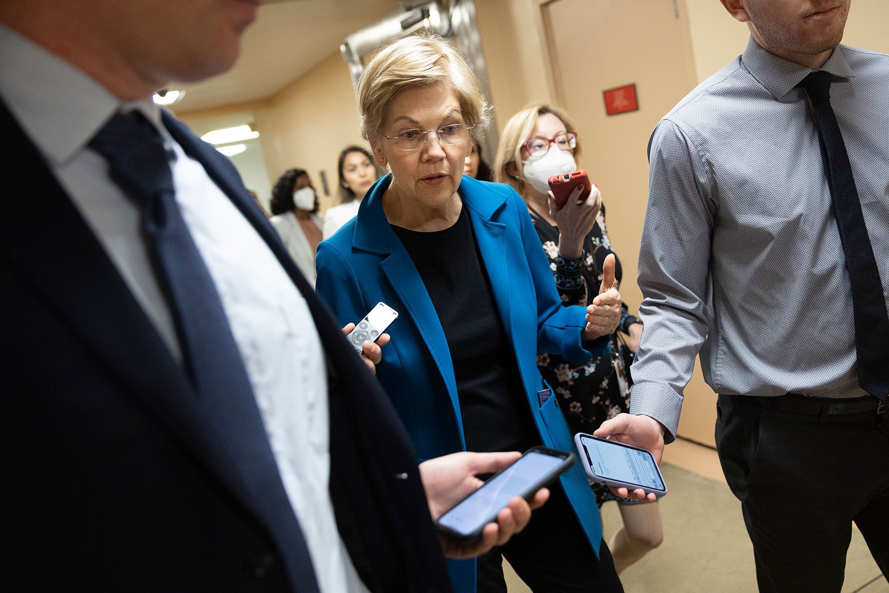 Sen. Elizabeth Warren walks down a corridor flanked by reporters.