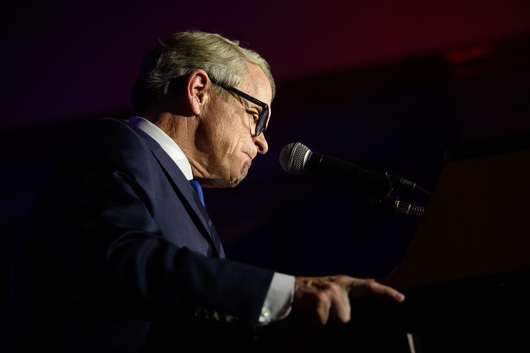 Ohio Governor Mike DeWine stands at a podium in a dark room.