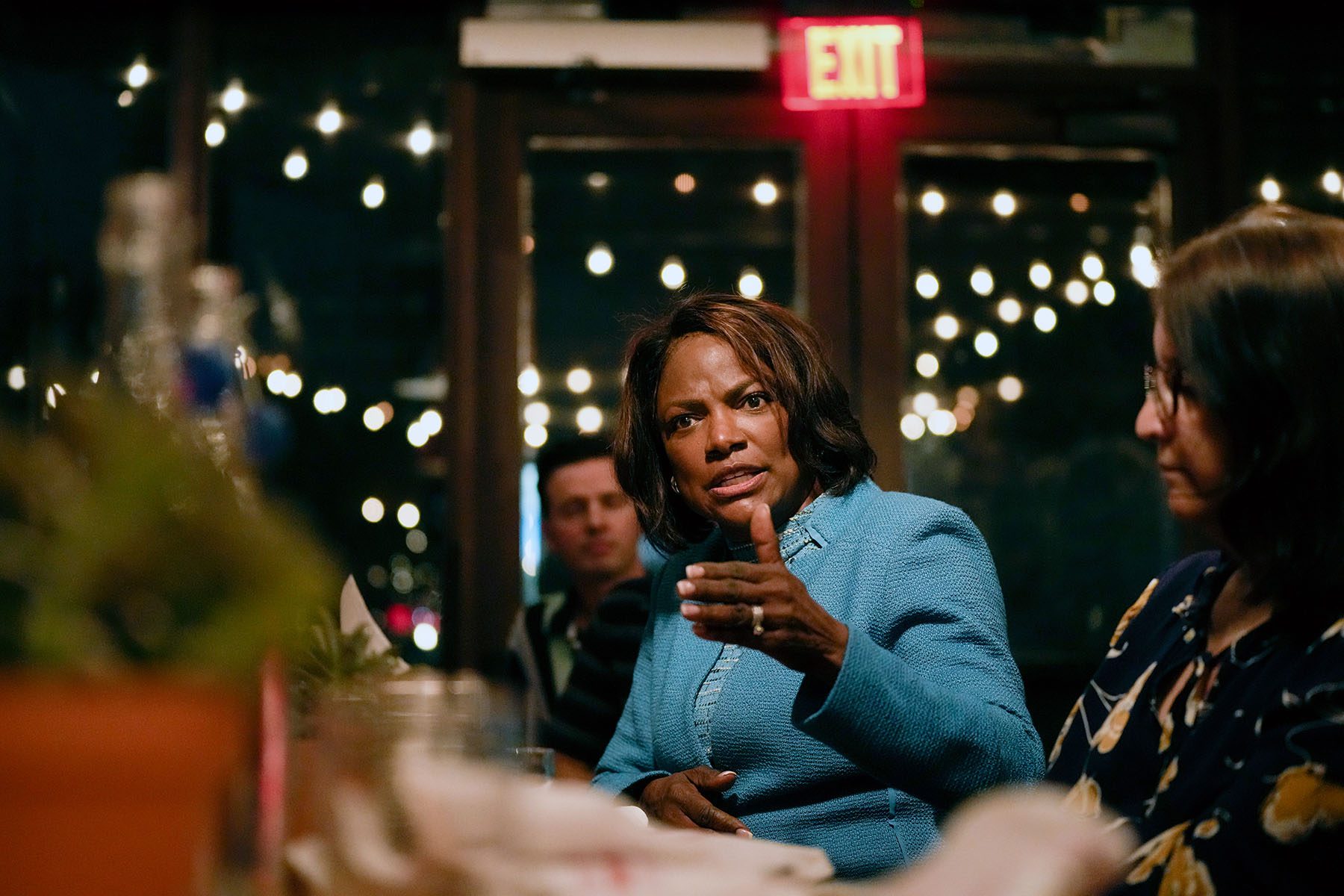 Val Demings sitting at a table with members of the Cuban-American community at a restaurant and gesturing while she speaks.