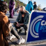 Carolyn Bourdeaux kneels to speak to supporters sitting on a curb. A sign that reads 