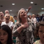 Christian evangelicals gesture and pray during a church service. Two young children are in the foreground of the image. One is looking at the camera, the other is looking away.