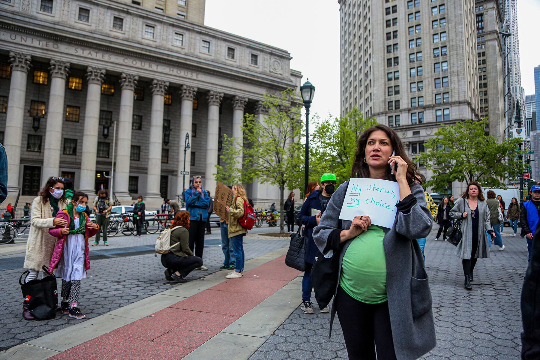 A visibly pregnant person holds a sign that reads "My Uterus, My Choice" as people gather to protest.