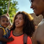 Nyla Harrison looks towards the Supreme Court as she holds her young daughter, Neeralena. Her partner stands next to the both of them, smiling as he looks at Nyla.