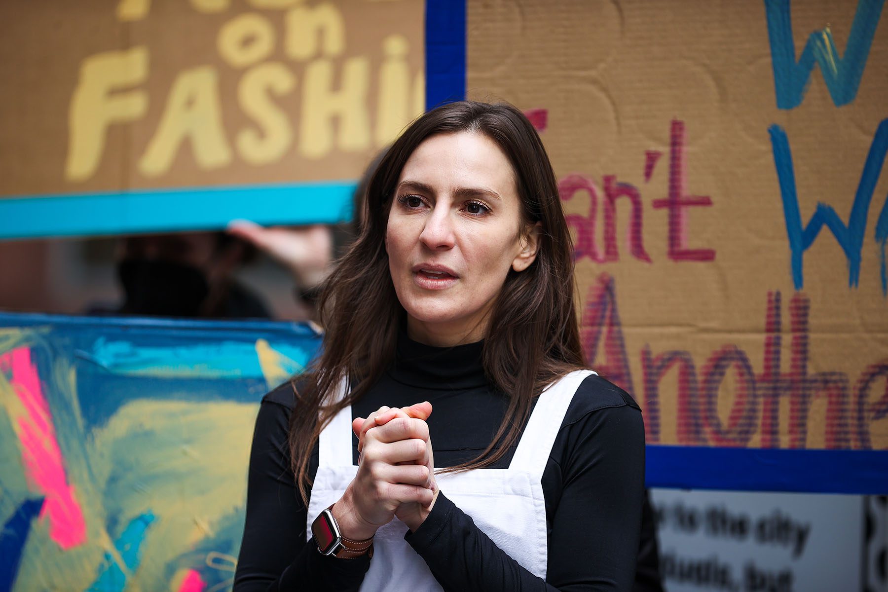 Alessandra Biaggi speaks as people holding signs demonstrate behind her.