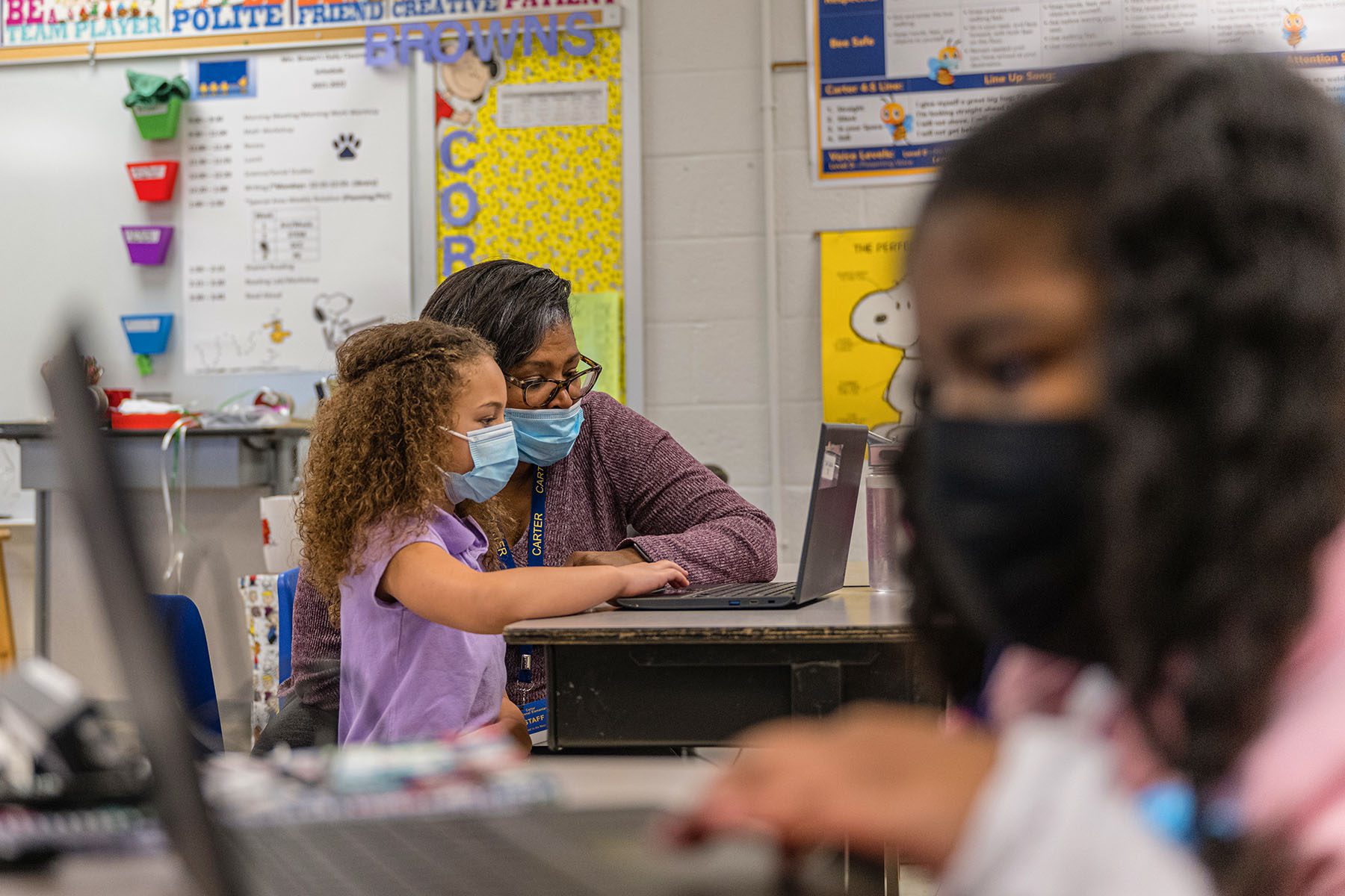 A second grade teacher, sits at a laptop computer with one of her students during a lesson.