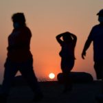 The sun sets behind people walking an afternoon hike.