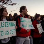 Students hold up signs that read 