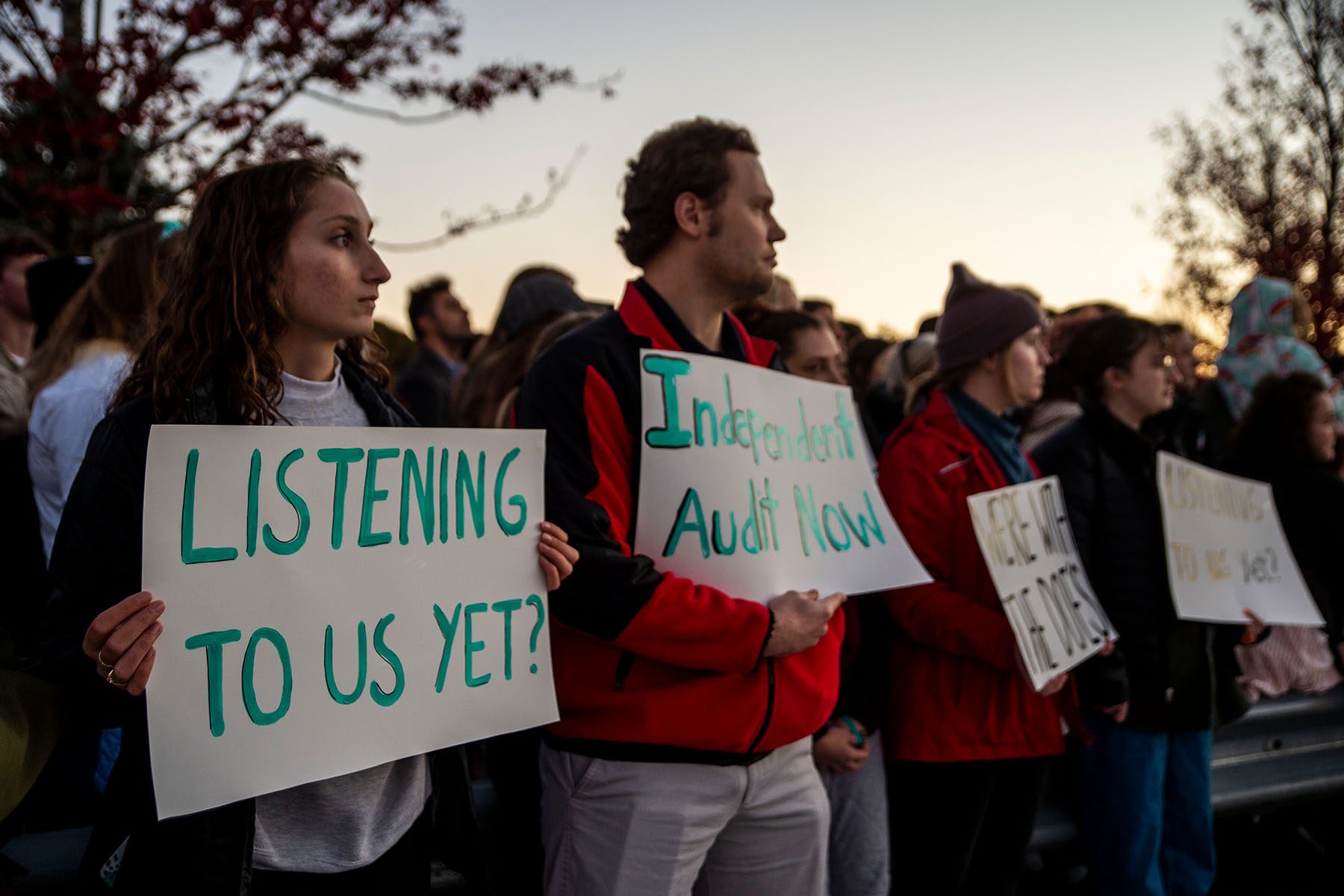 Students hold up signs that read "Listening to us yet?" and "Independent audit now."