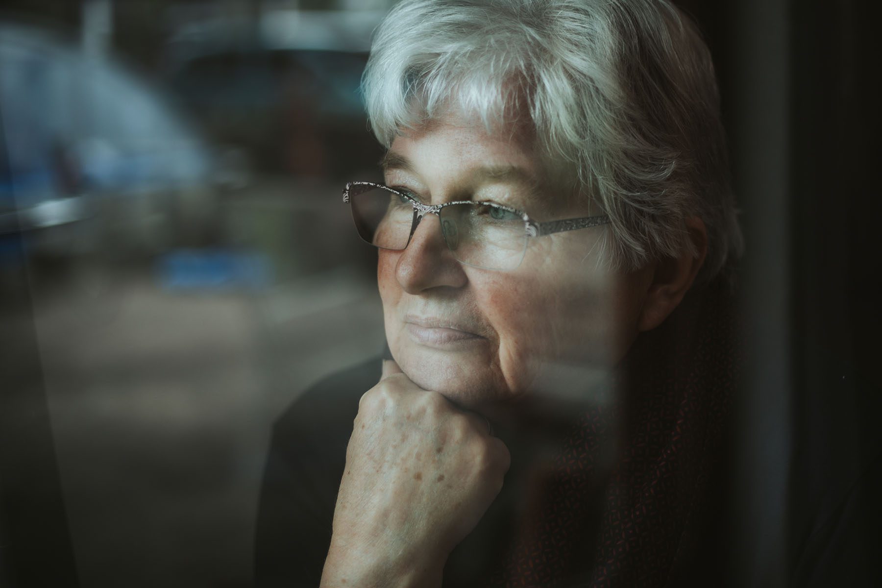 A pensive older woman looking out a window.