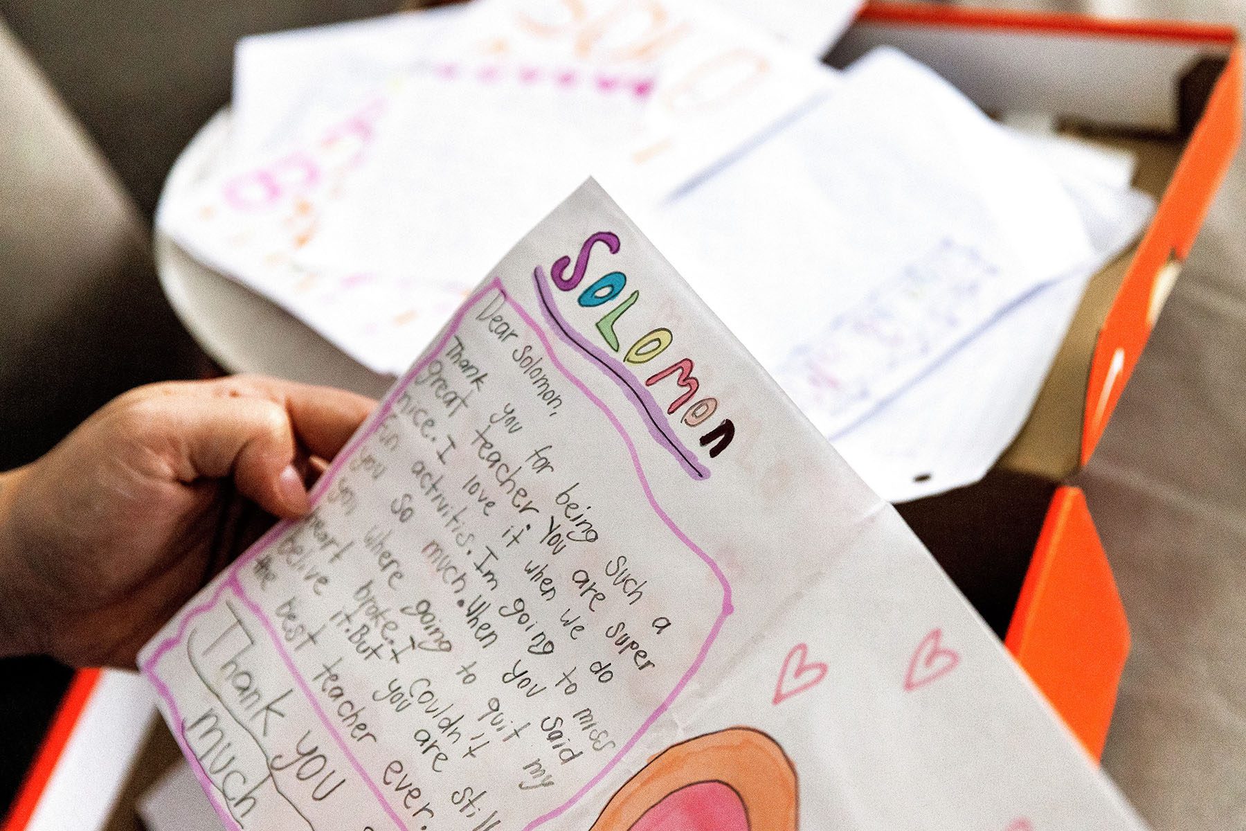 A teacher holds a letter from a former student that reads "Dear Solomon, thank you for being such a great teacher. You are super nice. I love it when we do fun activities. I'm going to miss you so much. When you said you were going to quit my heart broke. I coudn't believe it. But you are still the best teacher ever. Thank you so much."