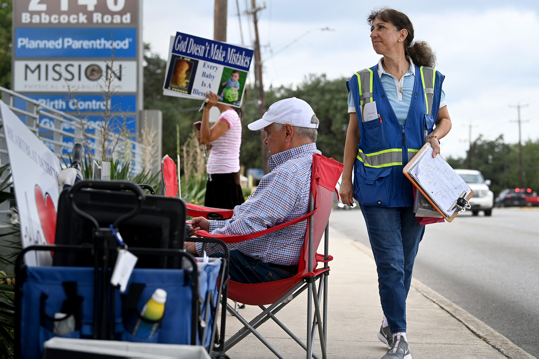 Cathy Nix is seen walking and holding a clipboard outside Planned Parenthood. A couple other anti-abortion protesters sit near the clinic.