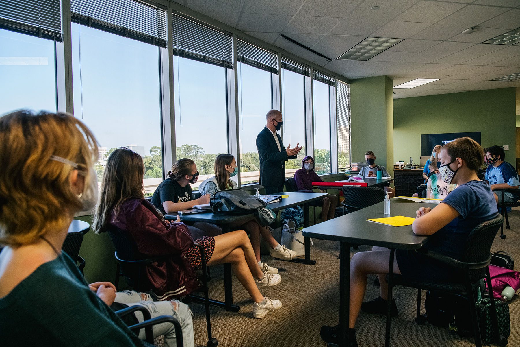 An instructor leads a classroom discussion. Students sit at table facing each other.