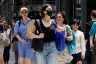 A group of three women walk on a crowded street.