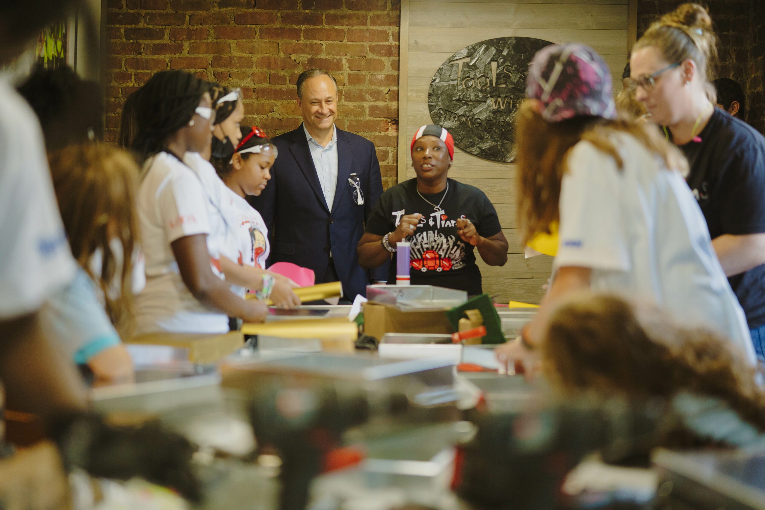 People stand around a table while listening to Second Gentleman Doug Emhoff.