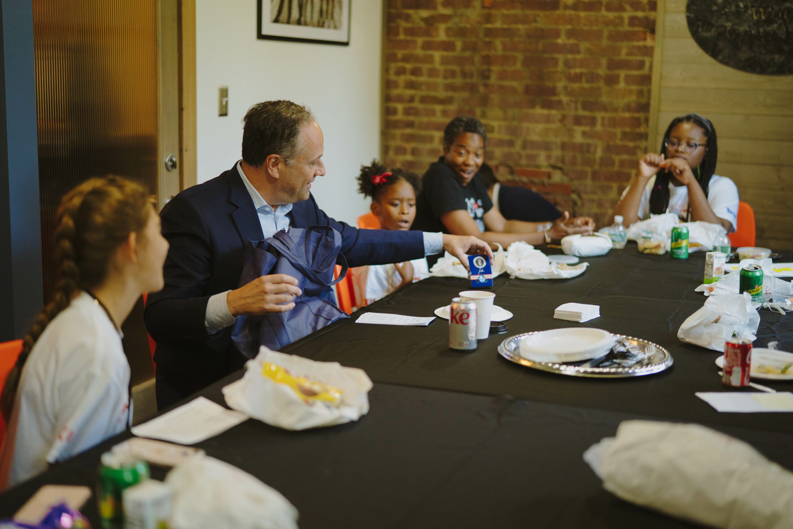 People sit at a table while listening to Second Gentleman Doug Emhoff.