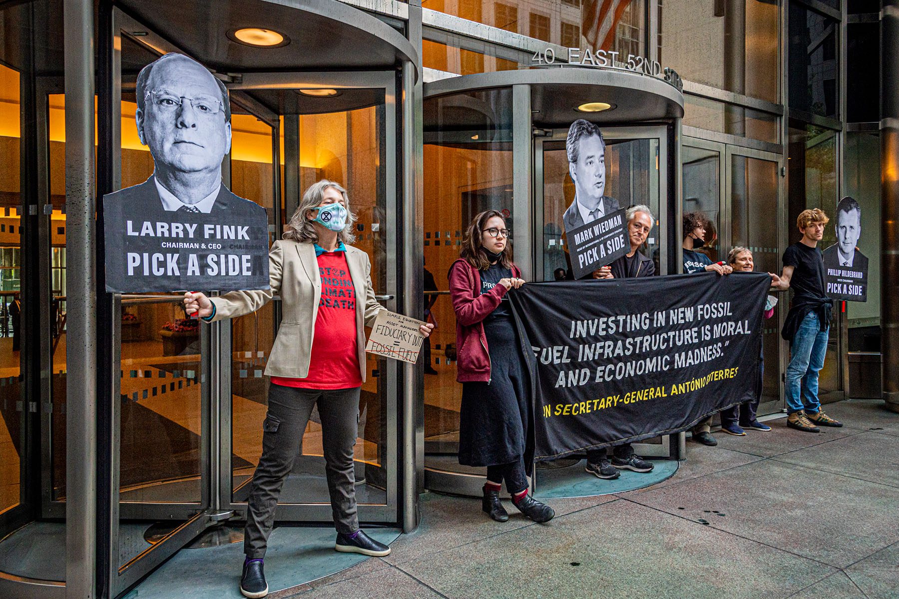 Climate activists hold signs and banners as they protest outisde BlackRock headquarters.