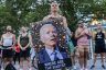 A protester holds a large image of President Biden looking bewildered and surrounded by question mark and thinking face emojis. Under the image are the words 