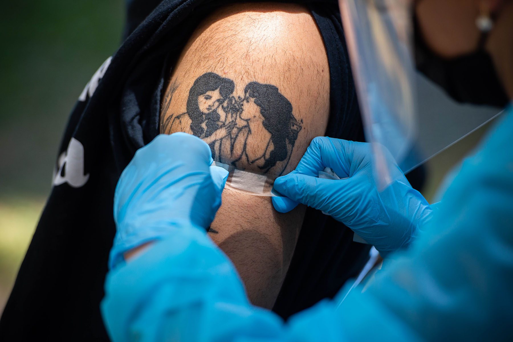 A nurse puts a bandaid on a man with a tattoo after administering his monkeypox vaccine.