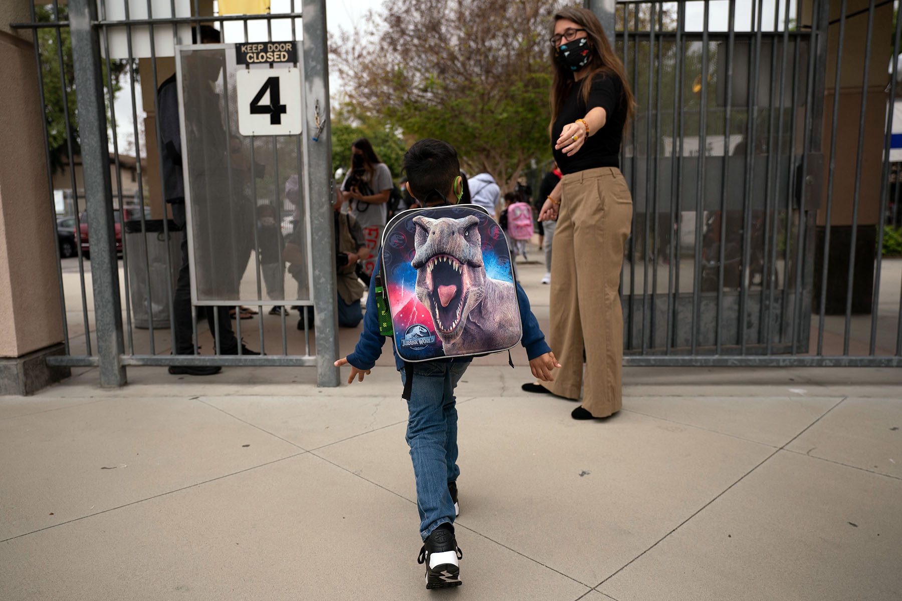 A kindergartener leaves Maurice Sendak Elementary School. He is wearing a large dinosaur themed backpack.