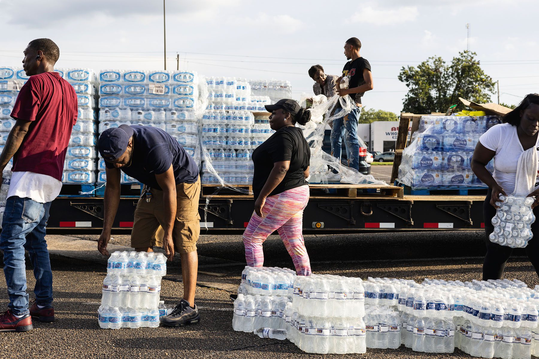 People grab packs of water bottles from a truck bed.